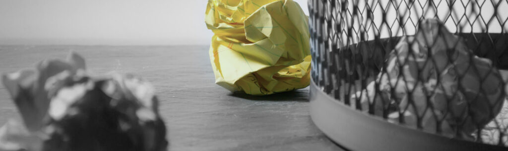 close up of gray mesh garbage can with crumpled yellow legal paper on the floor
