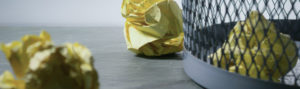 close up of gray mesh garbage can with crumpled yellow legal paper on the flooer