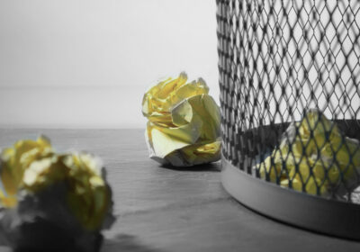 close up of gray mesh garbage can with crumpled yellow legal paper on the floor