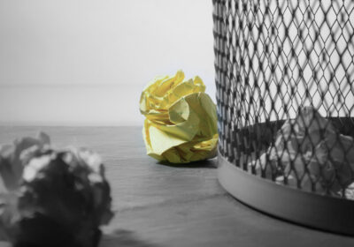 close up of gray mesh garbage can with crumpled yellow legal paper on the floor