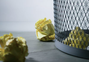 close up of gray mesh garbage can with crumpled yellow legal paper on the flooer